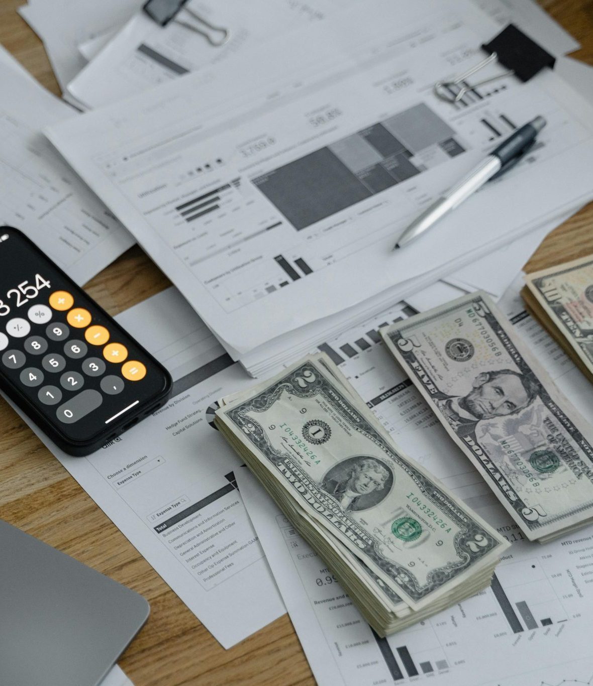 A desk with financial documents, currency, a laptop, and phone calculator.