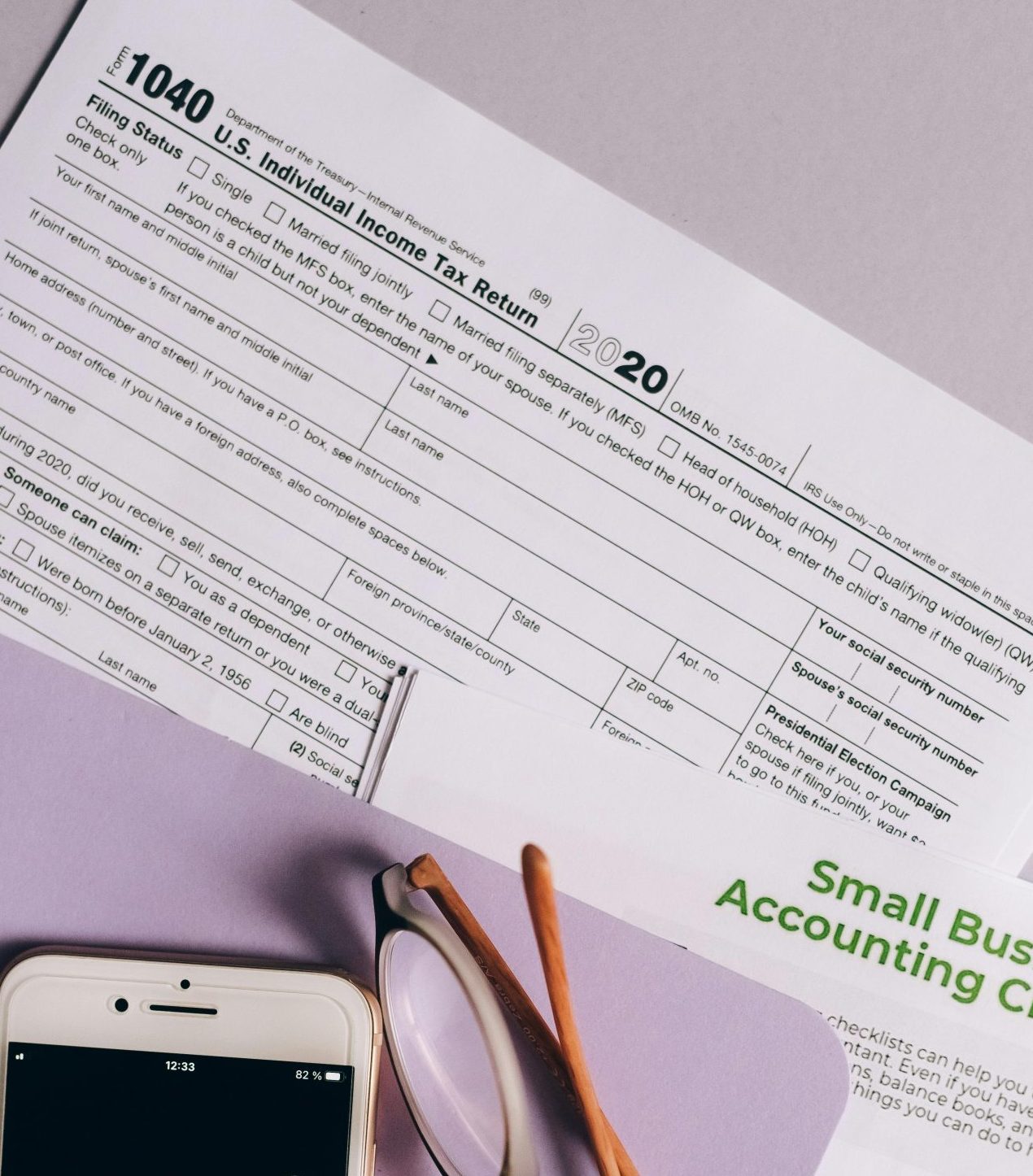 Flat lay of tax forms, checklist, smartphone, and glasses for small business accounting.